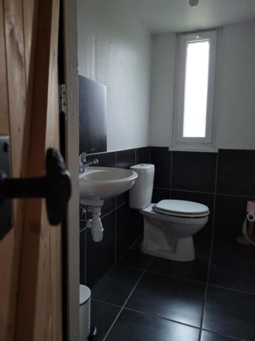 Salle de bains moderne au Chalet Cossu avec carrelage noir et blanc, lavabo rond, toilettes et vue sur le jardin
