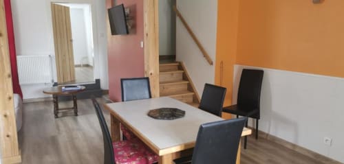 Open-plan living area in Gîte Terrasse cottage with dining table, black chairs, and mountain views via orange and white walls