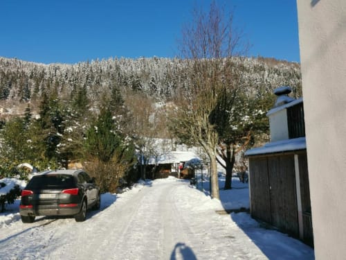 Snowy mountain village street with white cottage and parked car at Gîtes les Grandes voies, Le Ménil