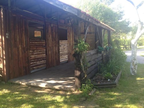 Chalet rustique en bois avec porche couvert aux Gîtes les Grandes voies, Le Ménil, entouré de jardins verdoyants et d'arbres