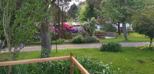 Vue luxuriante du jardin du Chalet Cossu avec arbustes fleuris, arbres, clôture en bois et pelouse soignée aux Gîtes les Grandes voies