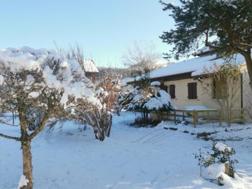 Snow-covered winter garden at Gîtes les Grandes voies cottage in Le Ménil, with house and evergreen trees