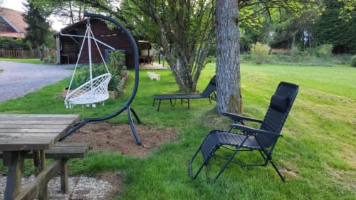 Cottage garden with hanging chair, lounge chair, tree shade, and gravel patio at Gîtes les Grandes voies