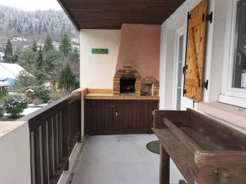 Terrasse couverte avec four à pizza en brique, mobilier en bois et vue sur les montagnes au gîte Les Grandes Voies au Ménil