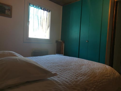 Bright bedroom in Gîte Jardin cottage with white bedding, teal wardrobe, and garden view window at Les Grandes Voies, Le