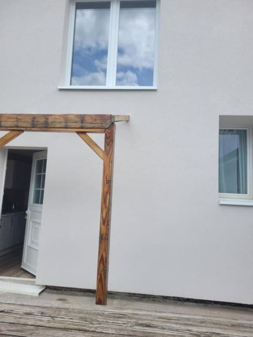 Wooden pergola entrance to white cottage at Gîtes les Grandes voies with garden view and blue sky