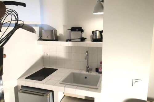 Petite kitchenette équipée dans le studio Denis & Virginie à Versailles avec cuisinière, évier et petits appareils sur fond blanc