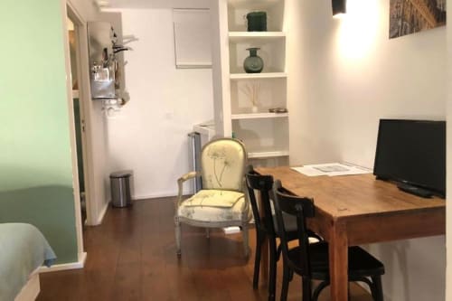 Espace de travail dans un studio du gîte Denis & Virginie à Versailles avec bureau en bois, chaise rembourrée et rangements intégrés.