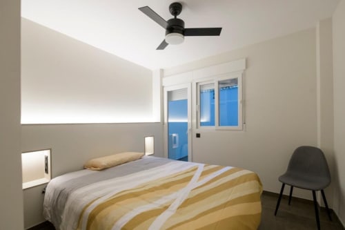 Habitación moderna en ML Apartments Valencia con cama, ventilador de techo, puertas correderas azules al balcón y silla negra