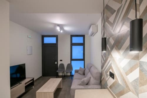Sala de estar moderna en Valencia con sofá gris, TV, zona de comedor y muro geométrico en ML Apartments