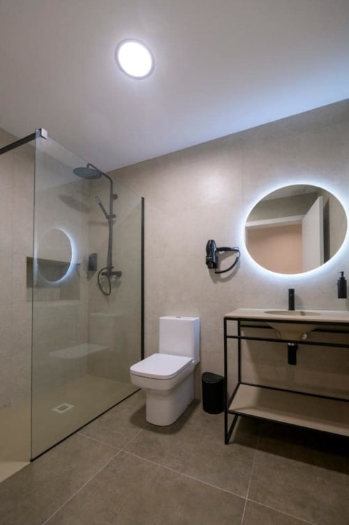 Baño moderno en ML Apartments Valencia con ducha abierta, espejo iluminado y accesorios negros contemporáneos