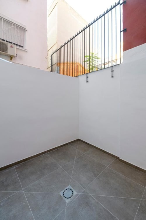 Patio minimalista en ML Apartments Valencia con piso de cerámica gris, paredes blancas y barandal metálico con vista al patio interior
