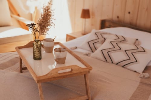 Cozy bedroom at Les Cabanes du Nideck with wooden bed tray, dried flowers, coffee cups, and patterned blanket