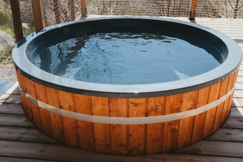Wooden hot tub with blue water on a deck at Les Cabanes du Nideck cottage in Oberhaslach