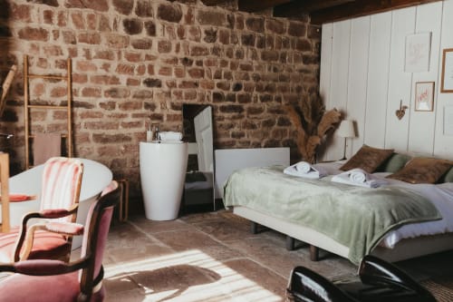 Rustic bedroom at Les Cabanes du Nideck cottage in Oberhaslach with exposed brick walls, bed, and vintage furnishings