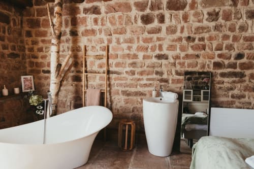 Rustic brick bathroom in Les Cabanes du Nideck cottage with freestanding tub, pedestal sink, and mountain views