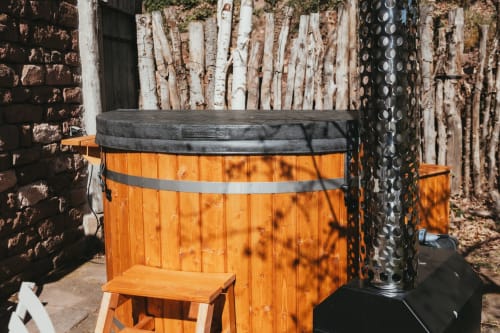 Wooden hot tub with black rim at Les Cabanes du Nideck cottage in Oberhaslach, surrounded by rustic stone and wooden