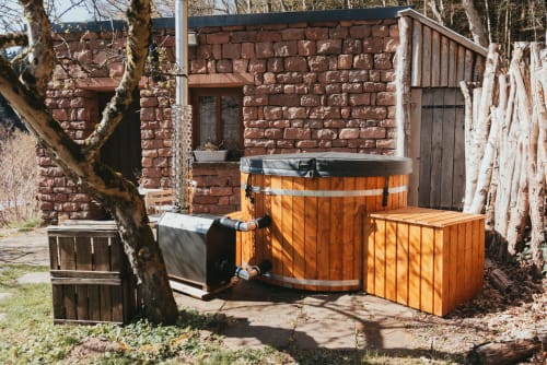 Wooden hot tub with steps at Les Cabanes du Nideck cottage in Oberhaslach, red brick buildings nearby
