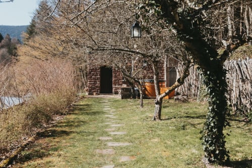 Stone cottage pathway at Les Cabanes du Nideck, Oberhaslach, with ivy-covered trees and mountains in background