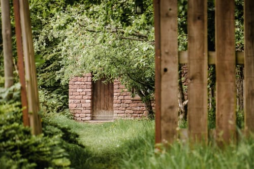 Rustic brick cottage nestled in lush greenery at Les Cabanes du Nideck, Oberhaslach, with wooden door and overgrown vines.