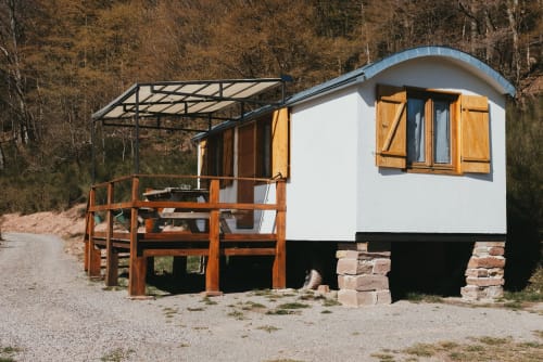 White cottage with wooden deck and metal canopy at Les Cabanes du Nideck in Oberhaslach, surrounded by autumn forest