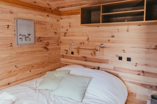 Wooden cabin bedroom with round bed, white bedding, and integrated sink at Les Cabanes du Nideck in Oberhaslach