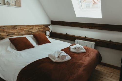 Cozy bedroom in Les Cabanes du Nideck cottage with white linens, brown pillows, rolled towels, and wooden beam ceiling in
