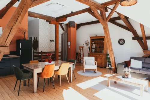 Open-plan cottage interior at Les Cabanes du Nideck with exposed wooden beams, dining table, kitchen, and living area with
