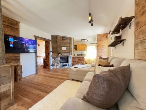 Cozy wooden chalet living room in Auronzo di Cadore with comfortable seating, TV, kitchenette, wooden shelves, and mountain