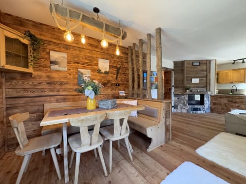 Rustic wooden chalet dining area with mountain views, pendant lights, and natural wood furnishings in Auronzo di Cadore