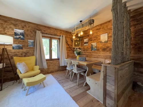 Wooden chalet interior in Auronzo di Cadore with yellow chair, dining table, and mountain views