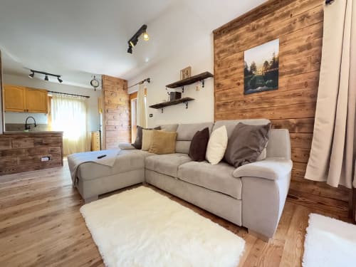 Cozy wooden chalet apartment in Auronzo di Cadore with beige sectional sofa, wood-paneled accent wall, and mountain views