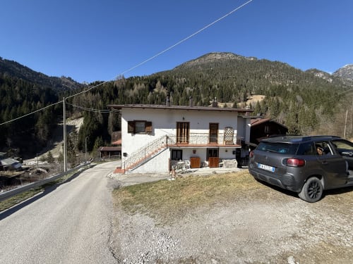 White chalet with balcony in Auronzo di Cadore mountains, parked car, forested peaks behind