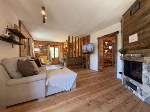 Rustic wooden chalet living room with fireplace, beige furniture, and mountain views in Val Comelico, Auronzo di Cadore