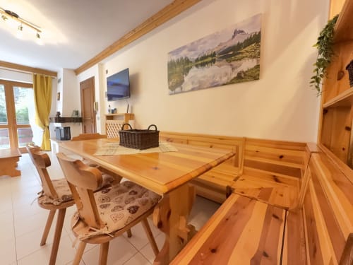 Tavolo da pranzo in legno con sedie in luminoso appartamento, opera d'arte con paesaggio montano, TV, vista sul balcone. Auronzo di Cadore