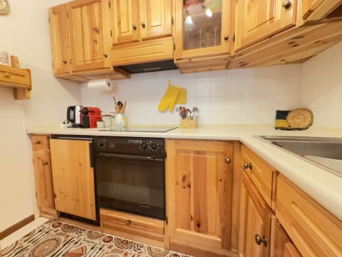 Cucina in legno in appartamento di montagna con stufa, lavello, ripiani bianchi e armadiature, ad Auronzo di Cadore