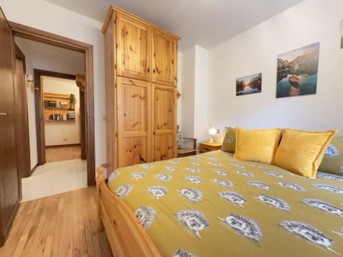 Camera accogliente con biancheria gialla a motivi, mobili in legno e vista sulle montagne nell'appartamento CIMABOSCO ad Auronzo di Cadore
