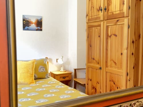 Accogliente camera da letto nell'appartamento CIMABOSCO di Auronzo di Cadore con biancheria gialla, mobili in legno e foto con vista montagna