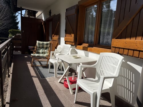 Terrazza soleggiata dell'appartamento in montagna con sedie di plastica bianche, tavolo da pranzo e sedia in legno con cuscini verdi con vista panoramica