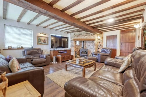 Spacious living room at Blackbrook Farmhouse in Colchester with exposed wooden beams, leather seating, fireplace, and
