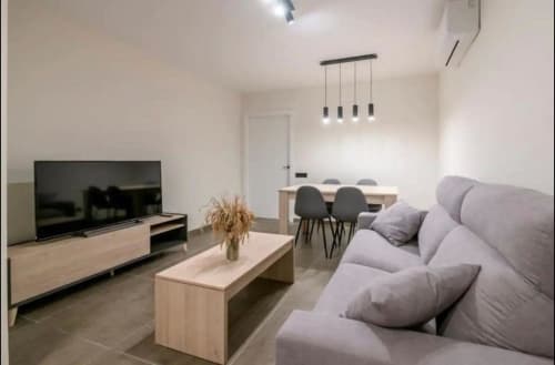 Sala de estar de apartamento moderno en Valencia con sofá gris, televisor de pantalla plana, comedor e iluminación de lámparas colgantes