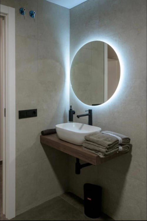 Baño moderno en ML Apartments Valencia con espejo ovalado iluminado, lavabo blanco tipo recipiente, grifería negra y toallas dobladas