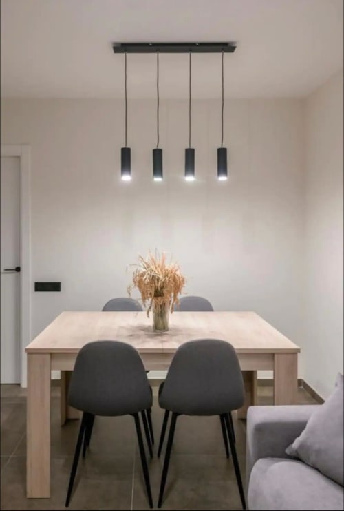 Zona de comedor moderna en ML Apartments Valencia con cuatro lámparas colgantes negras, mesa de madera clara y sillas oscuras