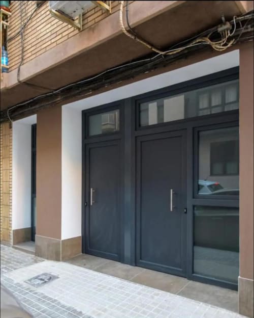 Puertas y ventanas modernas de vidrio negro en la entrada de ML Apartments en el barrio Roig Arena de Valencia, con diseño contemporáneo