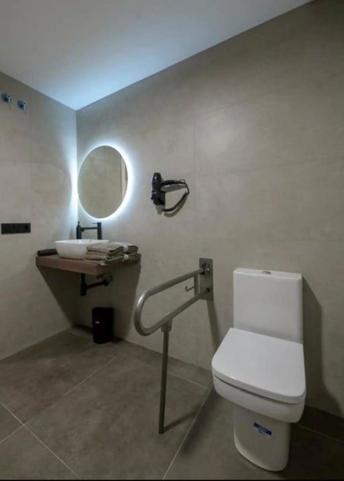 Baño moderno en ML Apartments Valencia con espejo ovalado iluminado, inodoro blanco, barra de apoyo accesible y lavabo tipo vasija
