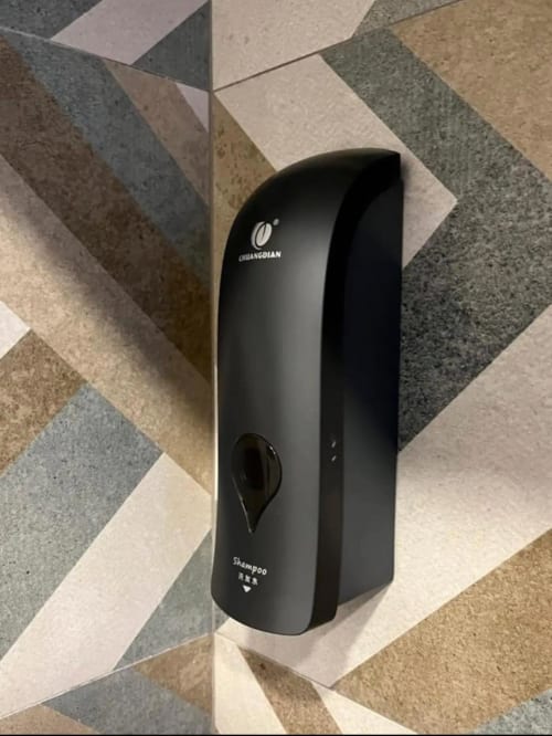 Dispensador de champú negro montado en pared del baño de ML Apartments Valencia con baldosas geométricas