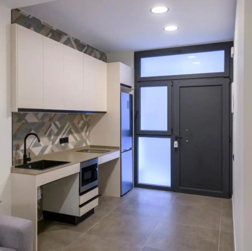 Cocina moderna en ML Apartments Valencia con armarios blancos, azulejos geométricos, pileta negra y electrodomésticos de acero inoxidable