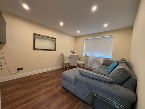 Modern living room with gray sofa, dining area, and flat-screen TV in England Furnished Homes villa, High Wycombe
