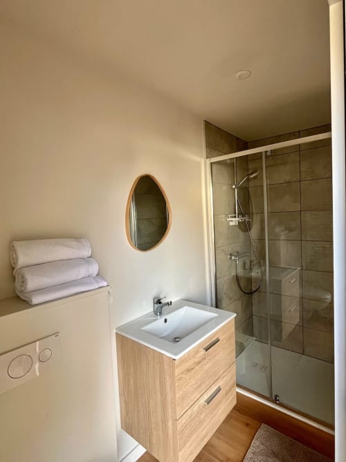 Salle de bain moderne du studio Haut Chalet aux Logis du canal avec vanité en bois, miroir ovale et douche à l'italienne