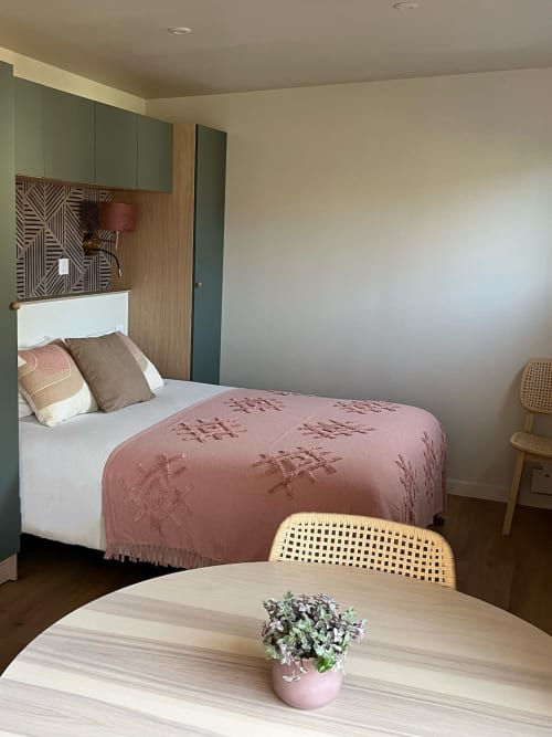 Chambre studio moderne aux Logis du Canal avec lit à literie rose, mobilier vert, finitions bois et coin repas